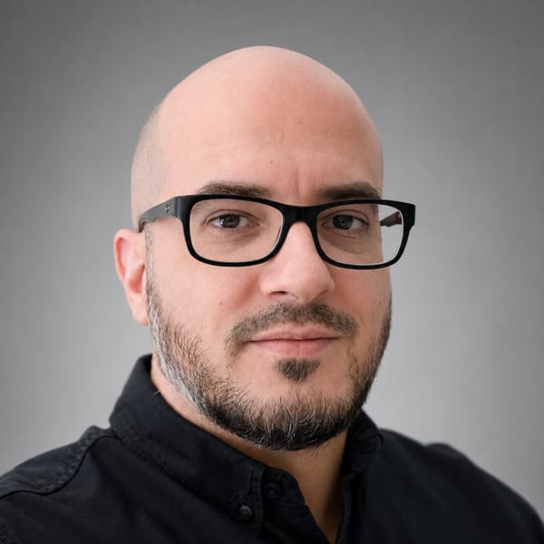 Portrait of Rakan Brahedni, founder of MADNESS, wearing glasses and a dark button-up shirt against a neutral background.